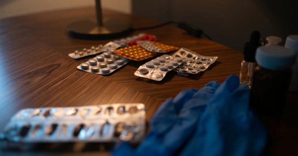 ایک میز پر بکھرے ہوئے ادویات کے مختلف پتے (Blister packs) اور گولیاں، جو گھر پر ادویات کے صحیح استعمال اور انتظام کی اہمیت کو ظاہر کرتے ہیں۔